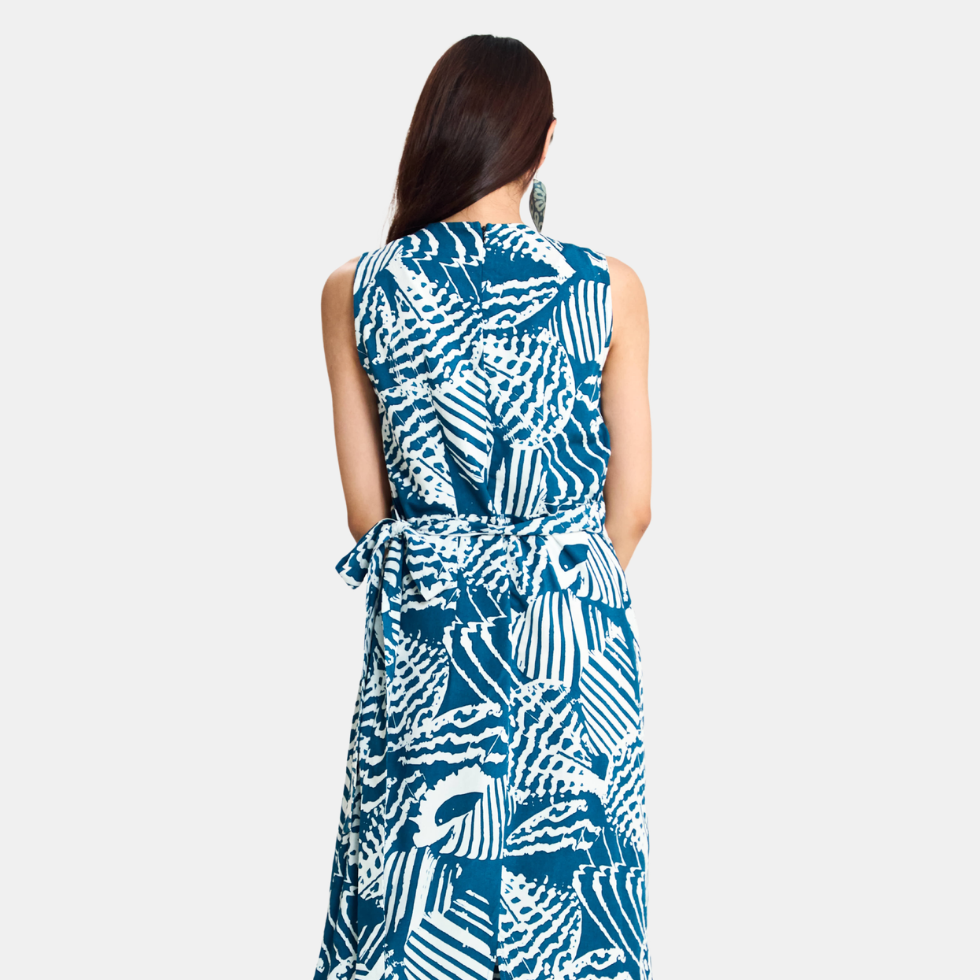 A woman viewed from the back wearing a sleeveless wrap-style dress with a bold blue and white abstract pattern, set against a plain light gray studio background.