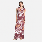 A woman modeling a sleeveless wrap-style maxi dress with a tie waist and an abstract light maroon and off-white pattern, set against a plain light gray studio background.