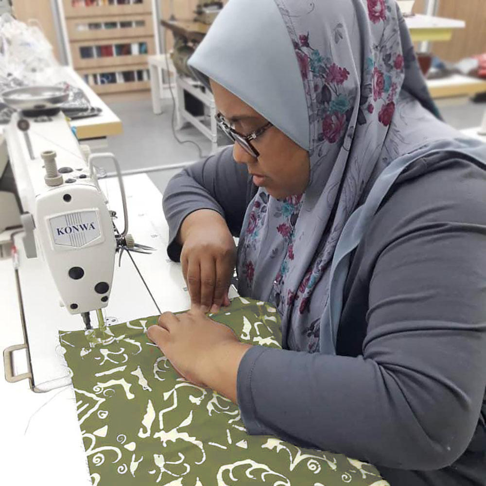 An artisan skillfully engaged in the sewing process of authentic batik fabric, showcasing precision and dedication to the artistry of this traditional craft