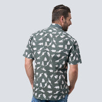 a man standing in front of a white wall while wearing a batik shirt in olive dinosaurs pattern