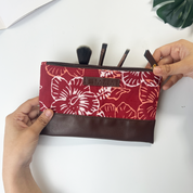 Floral-patterned makeup bag with brown base held by hands on a white background