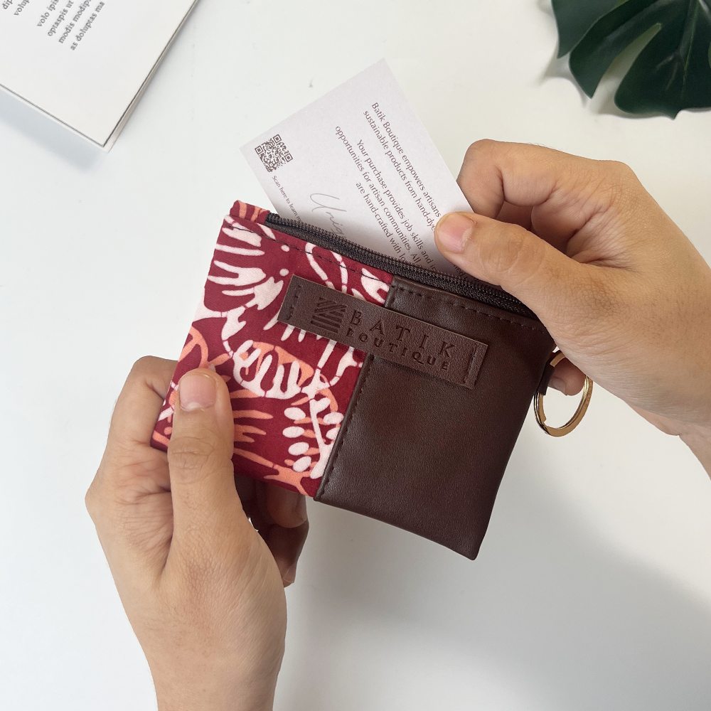 Person holding a small pouch with a floral pattern and brown leather section, featuring the brand 'Batiki Boutique'.