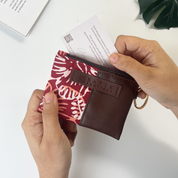 Person holding a small pouch with a floral pattern and brown leather section, featuring the brand 'Batiki Boutique'.