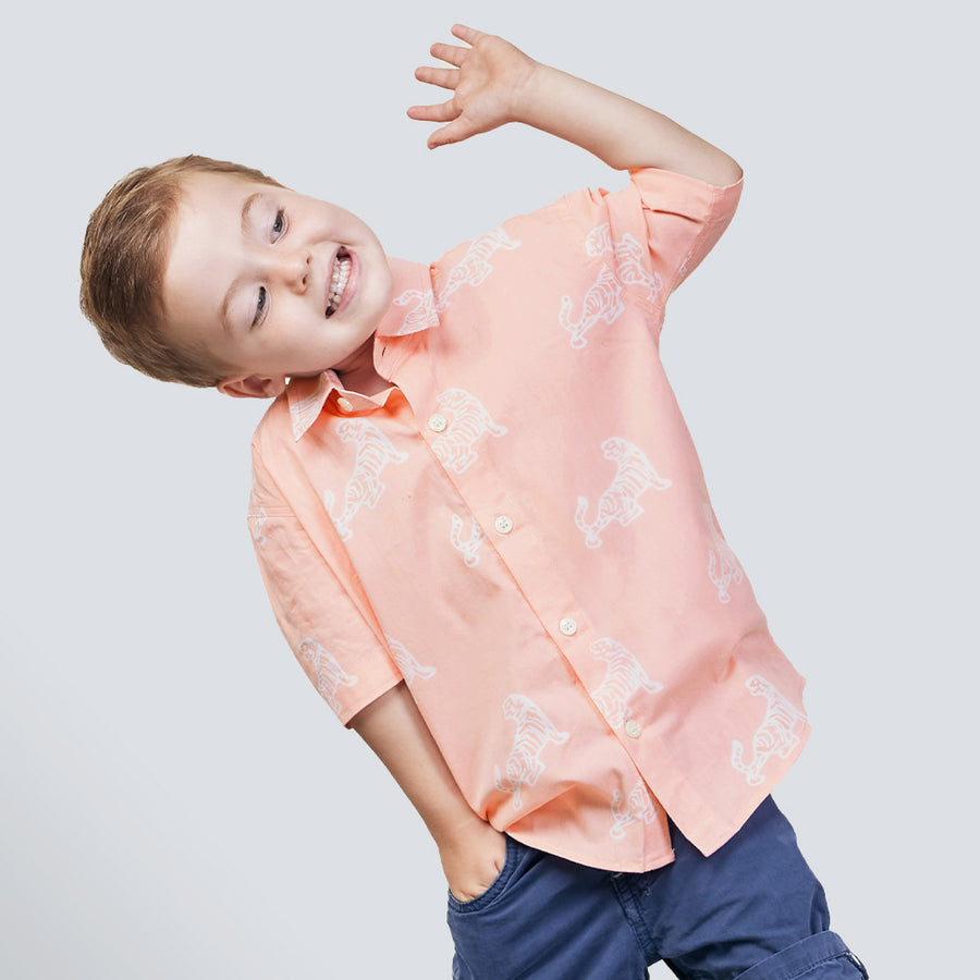 a boy posing in front of a white wall while wearing a peach tiger batik shirt