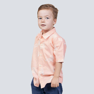 a boy standing in front of a white wall while wearing a peach tiger batik shirt