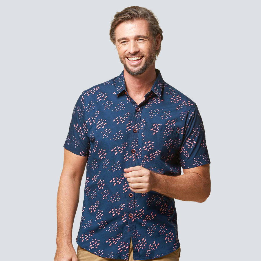 a man posing in front of a white wall while wearing a batik shirt in pink seeds pattern