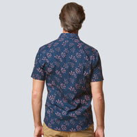 a back view of a man wearing a batik shirt in pink seeds pattern in front of a white wall