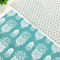 a photo showcasing two reversible batik placemats in the print turquoise pineapple