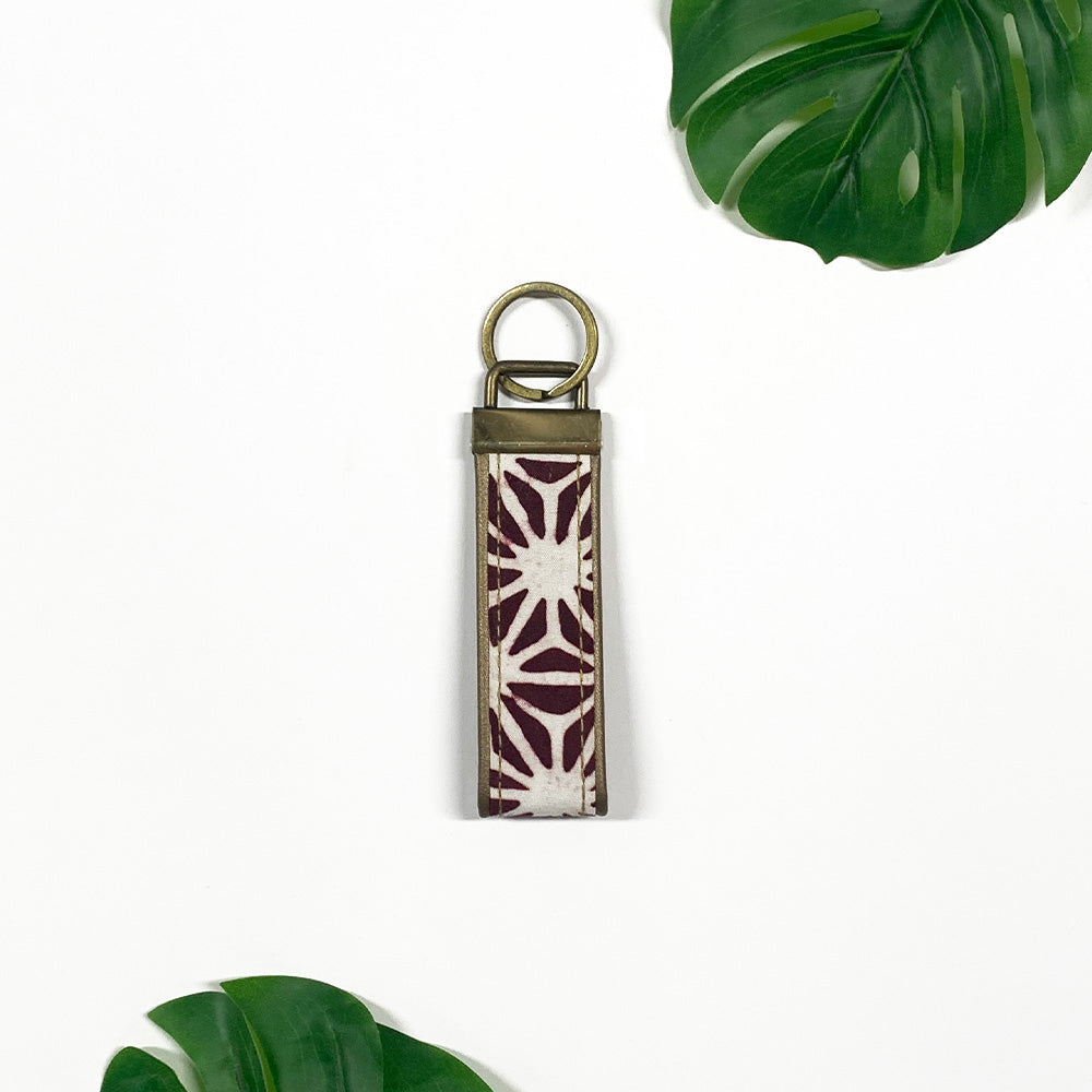 a lifestyle picture of a key fob made of batik in the pattern plum firework against a neutral background and with tropical leaves as decorations