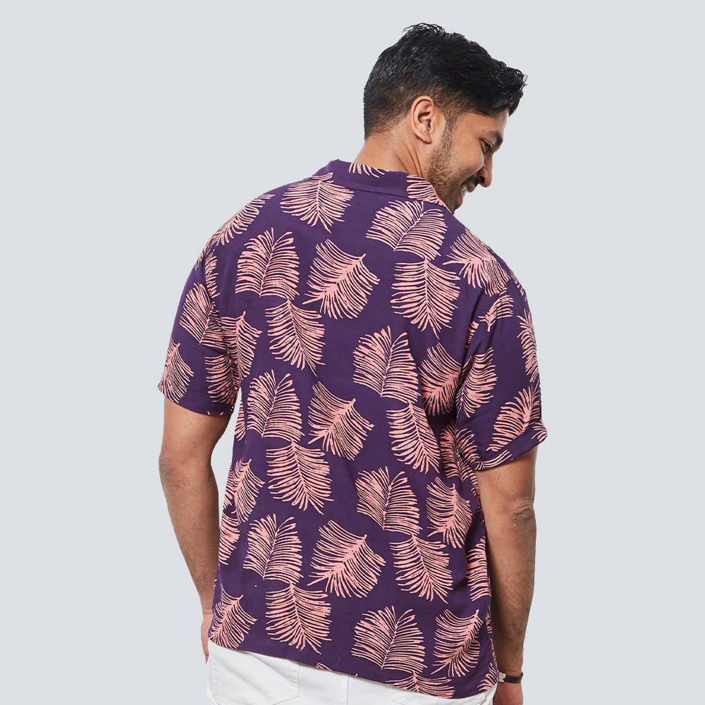 a man standing in front of a white wall while wearing a batik shirt in purple sawit pattern