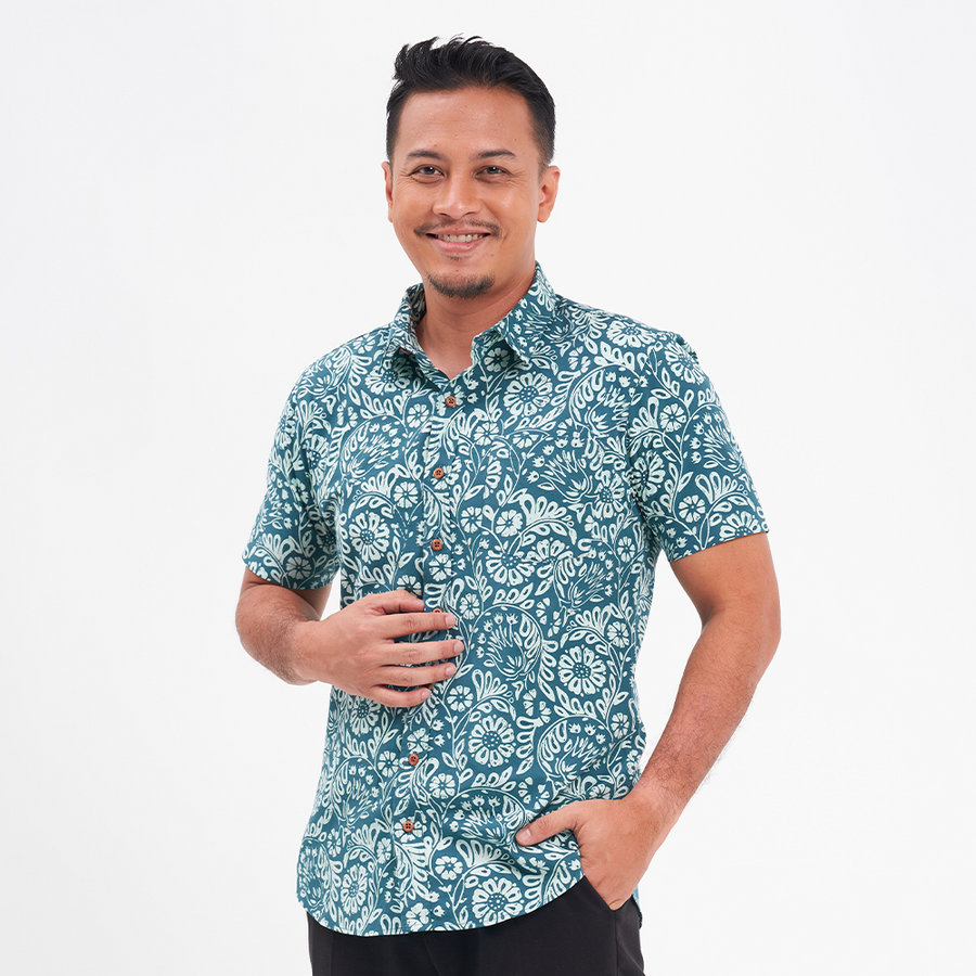 a male model posing against a white background while wearing a batik shirt in the pattern teal ukir