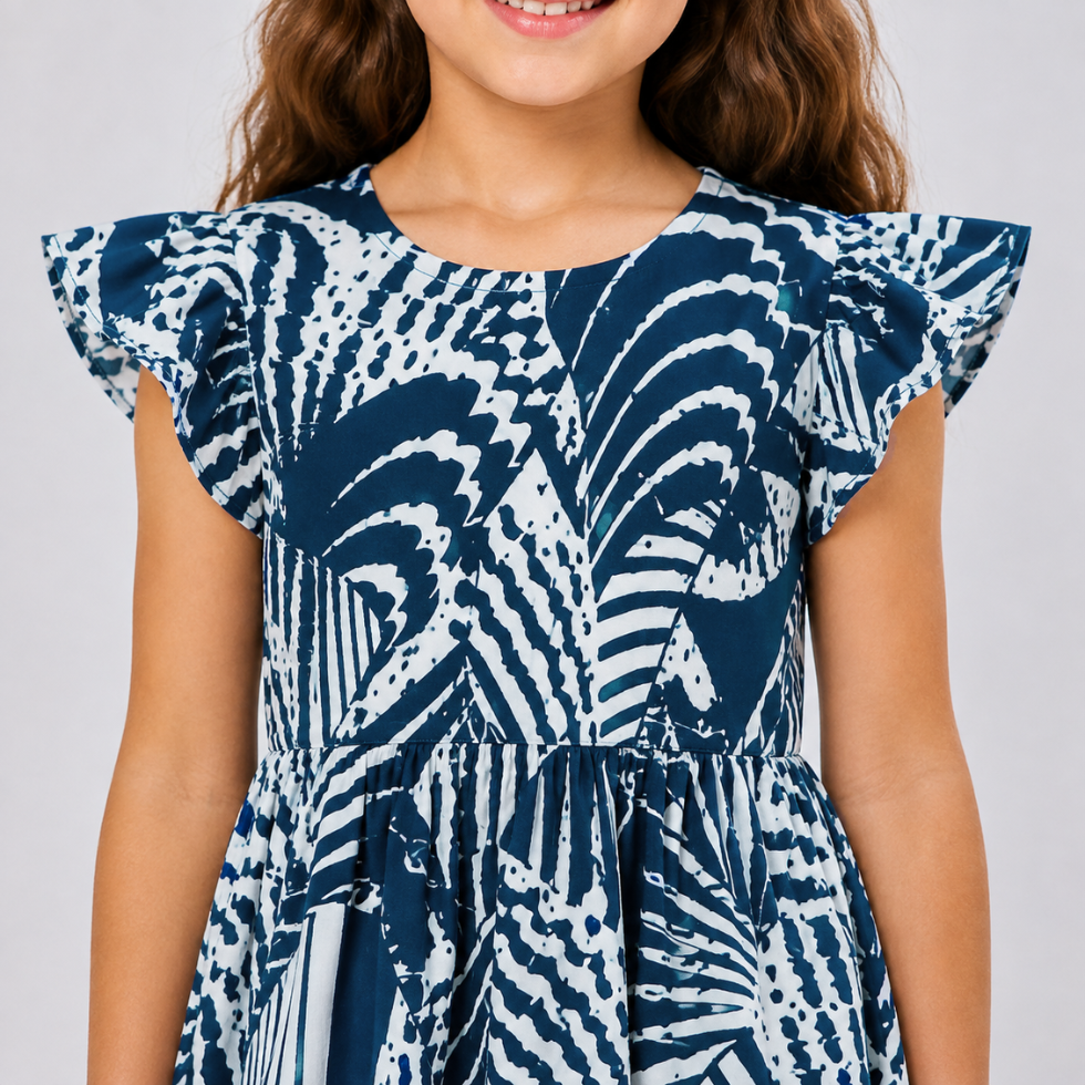 A child wearing a navy blue and white patterned dress with ruffled cap sleeves and a gathered waist, shown against a light gray studio background.