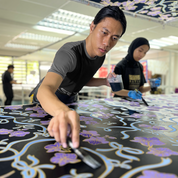 an artisan in the process of coloring in batik in the pattern sapphire fleur