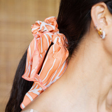 a woman styling batik scrunchie in peach fern with background of rattan divider