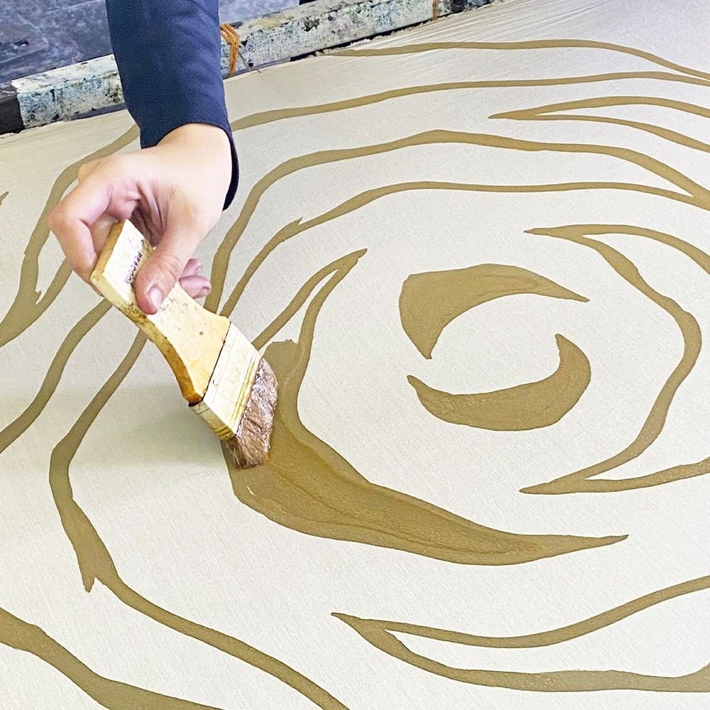 Hand applying gold paint to a surface with a swirling pattern