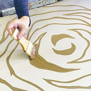 Hand applying gold paint to a surface with a swirling pattern