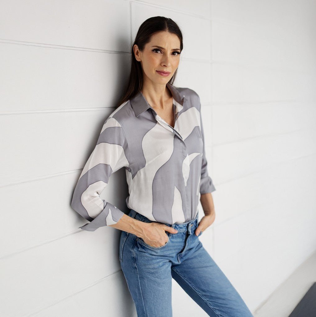 Woman wearing a patterned shirt and jeans against a white wall