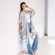 Woman wearing a long, patterned gray and white kimono-style garment against a white wall. SilverRose_Kimono-Lifestyle.