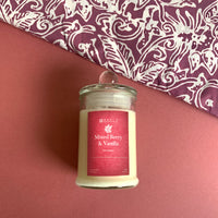 a mixed berry and vanilla scented soy candle in front of a wall accompanied by batik patterned similarly to the candle