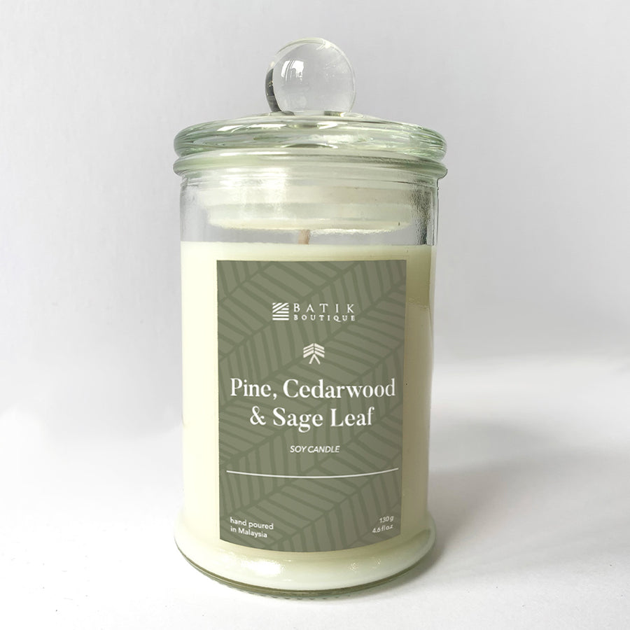 a pine, cedarwood and sage leaf scented soy candle sits in front of a white wall
