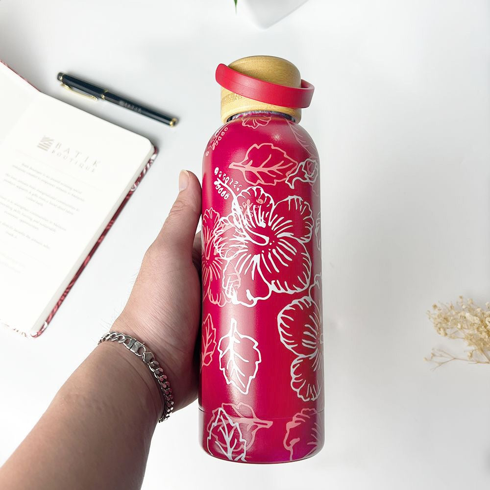 Hand holding a red water bottle with floral design on a white surface
