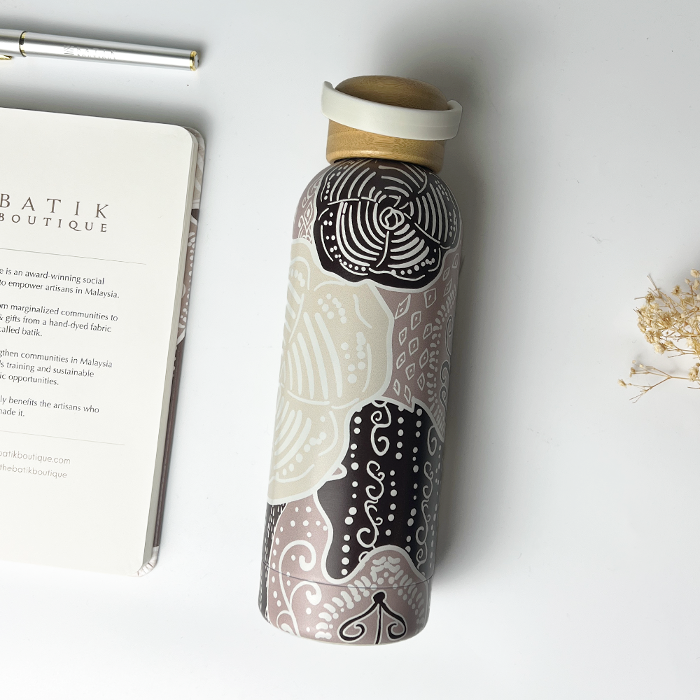 Decorative water bottle with batik design on a white surface next to a notebook and pen.