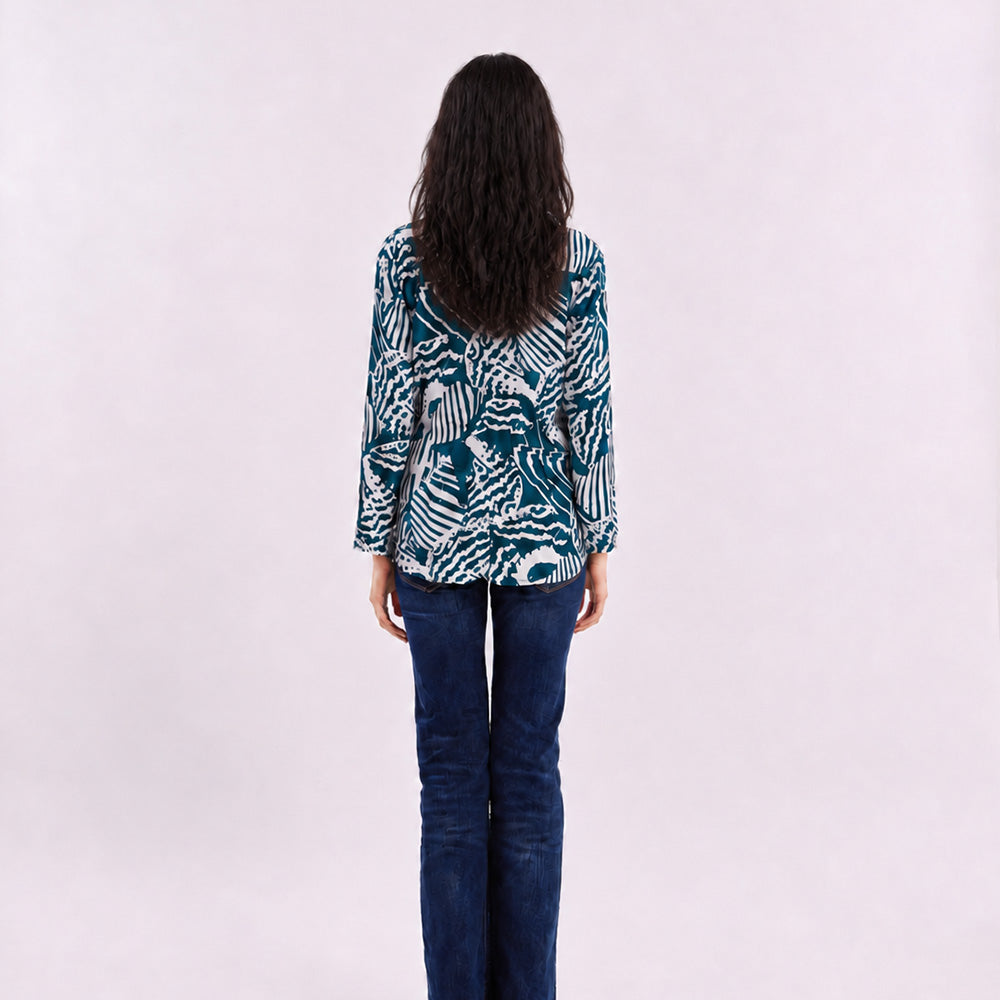 A woman wearing a blue kebaya top with a blue shell pattern, facing her back on a white background.
