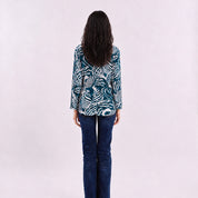 A woman wearing a blue kebaya top with a blue shell pattern, facing her back on a white background.
