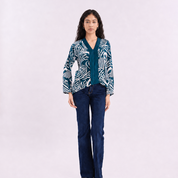 A woman wearing a blue kebaya top with a blue shell pattern, on a white background.