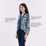 A woman wearing a blue kebaya top with a blue shell pattern, on a white background with top details.