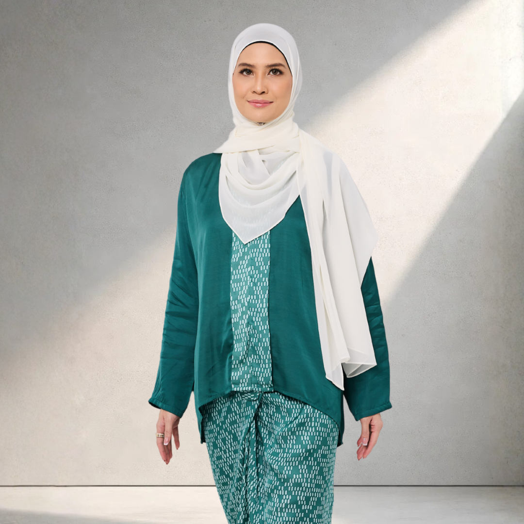 Woman wearing a green and white outfit with a hijab against a neutral background