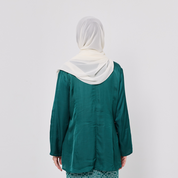 Person wearing a green top and white hijab on a plain background
