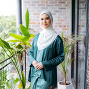Woman in a teal traditional outfit standing in front of a brick wall with plants.