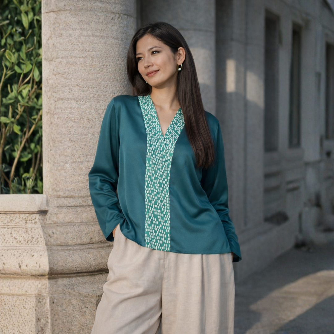 Woman wearing a teal blouse with a patterned front panel standing against a building.