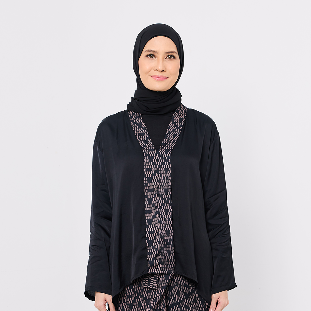 Woman wearing a black hijab and black outfit with a patterned scarf on a white background