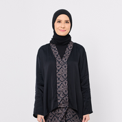 Woman wearing a black hijab and black outfit with a patterned scarf on a white background