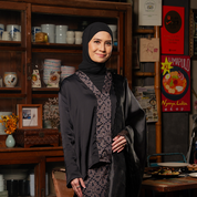 Woman wearing a black hijab and dark clothing in a room with wooden furniture and decor.