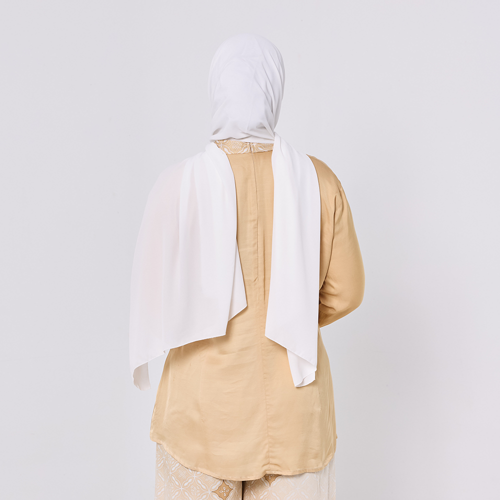 Person wearing a beige outfit with a white headscarf on a plain background