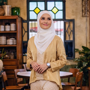 Woman wearing a beige top and white hijab in a restaurant setting