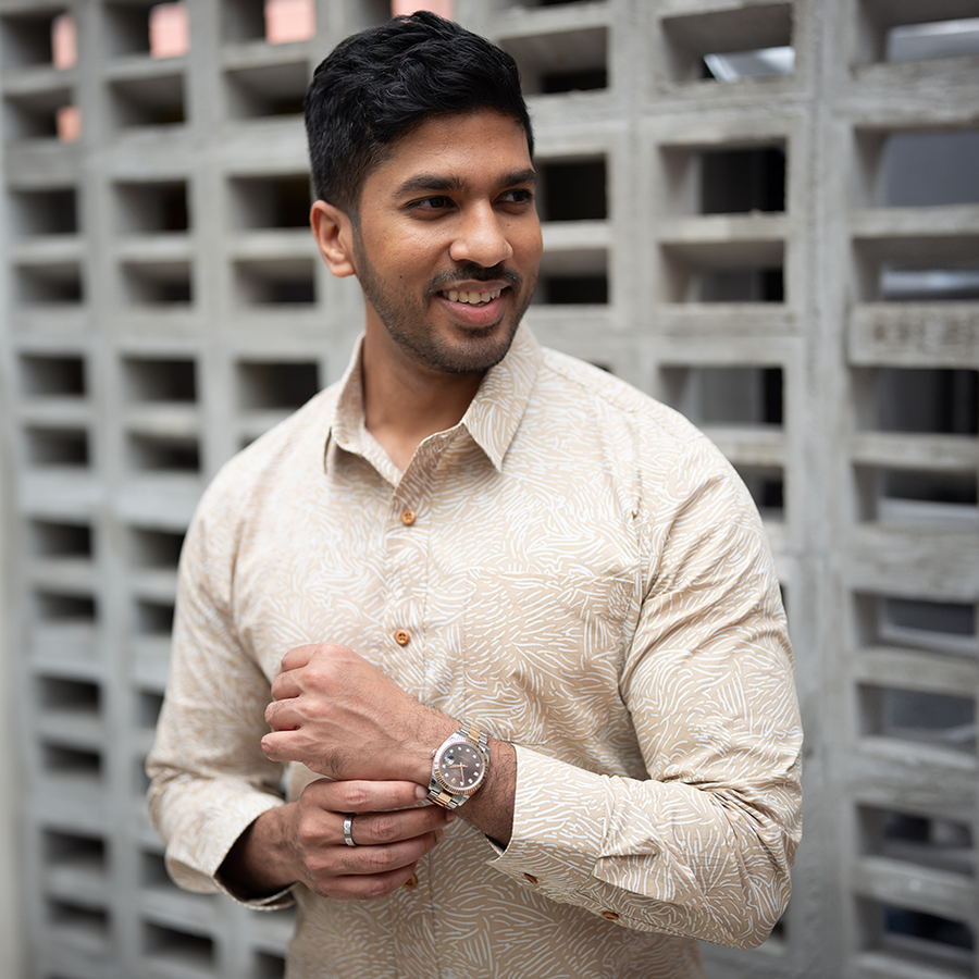 A man is wearing long sleeve batik shirt in tan driftwood with brick as a background
