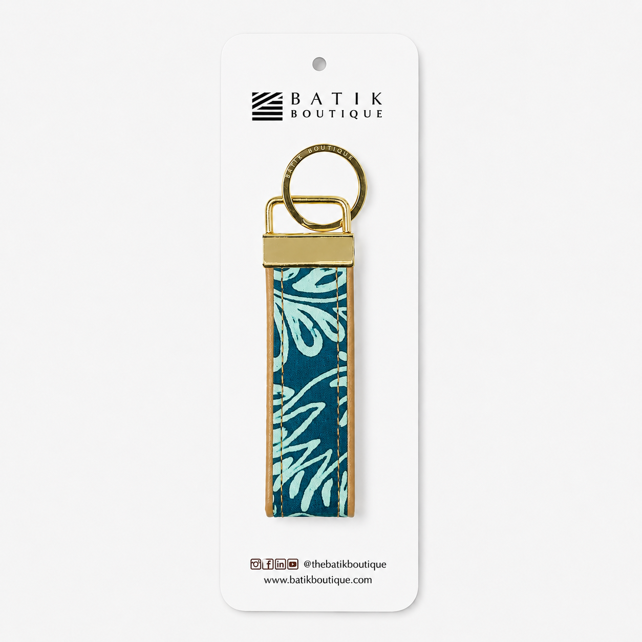A rectangular leather keychain strap featuring a teal and light blue floral batik pattern, finished with a brass key ring and metal hardware, in a packaging