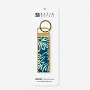A rectangular leather keychain strap featuring a teal and light blue floral batik pattern, finished with a brass key ring and metal hardware, in a packaging
