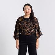 Woman wearing a black and gold patterned top with black pants on a white background
