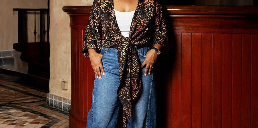 Woman standing in a stylish outfit with a patterned top and jeans in an indoor setting.