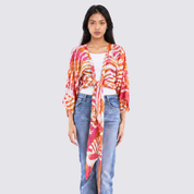 Woman wearing a colorful kimono-style jacket and jeans on a plain background
