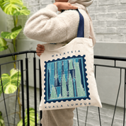 Woman carrying totebag with the Kuala Lumpur print on it, blue-ish tones