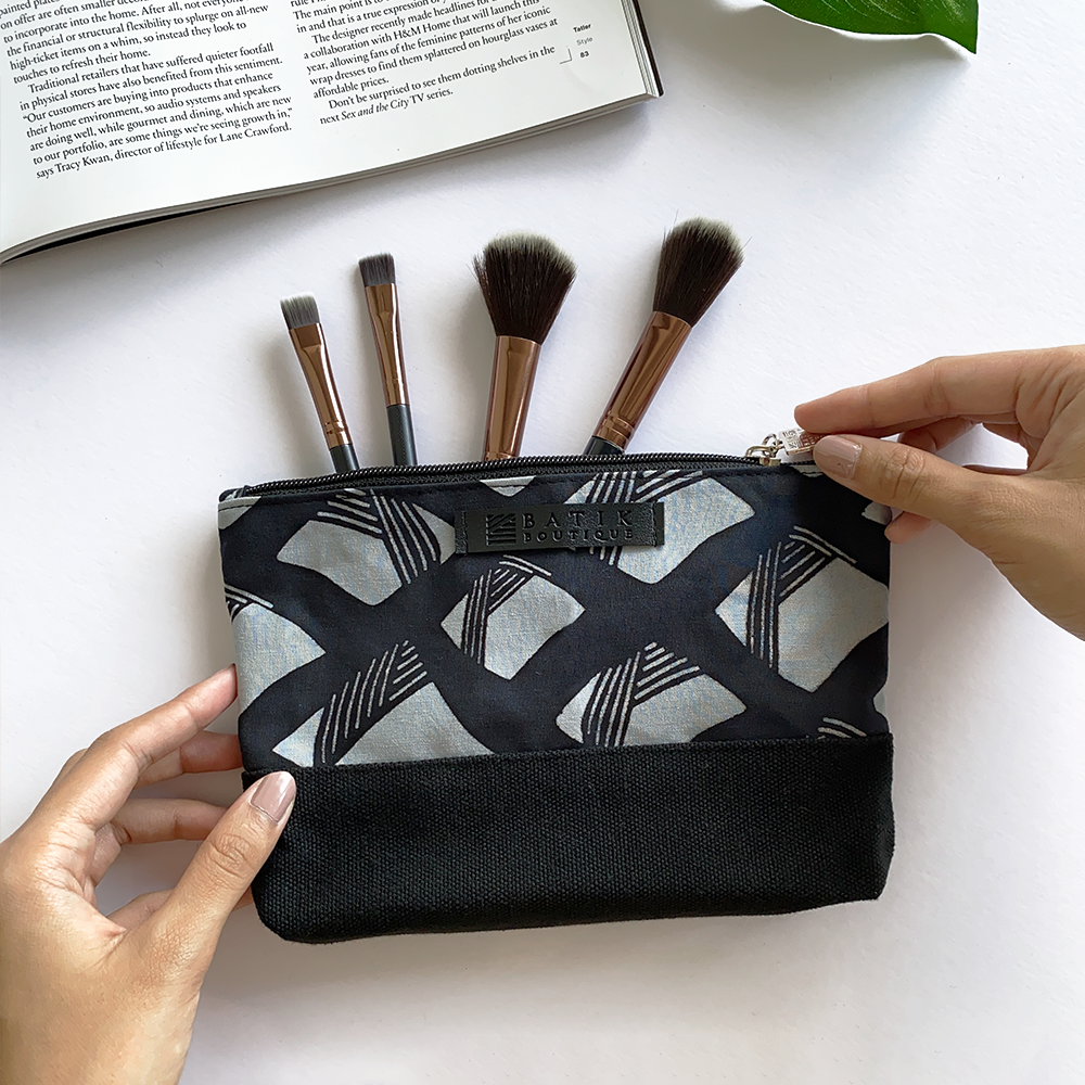 a lifestyle photo of a batik zip pouch made of batik in the pattern black nasi lemak against a neutral background