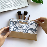 a flatlay photo of batik zip pouch in grey floral pattern with white background and a hand holding the pouch