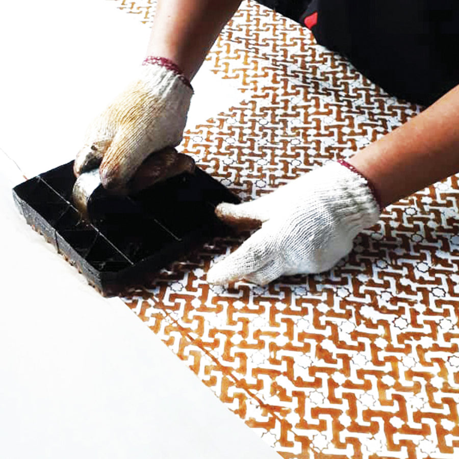 a photo of an artisan in the process of blocking batik in the pattern arabesque
