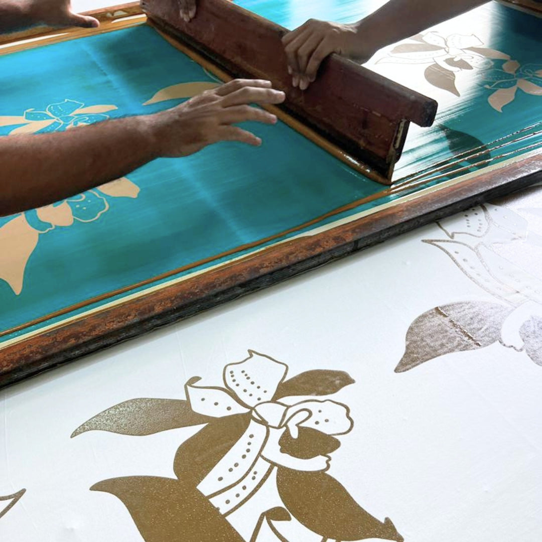Screen printing process with a person using a squeegee on a screen with floral designs.